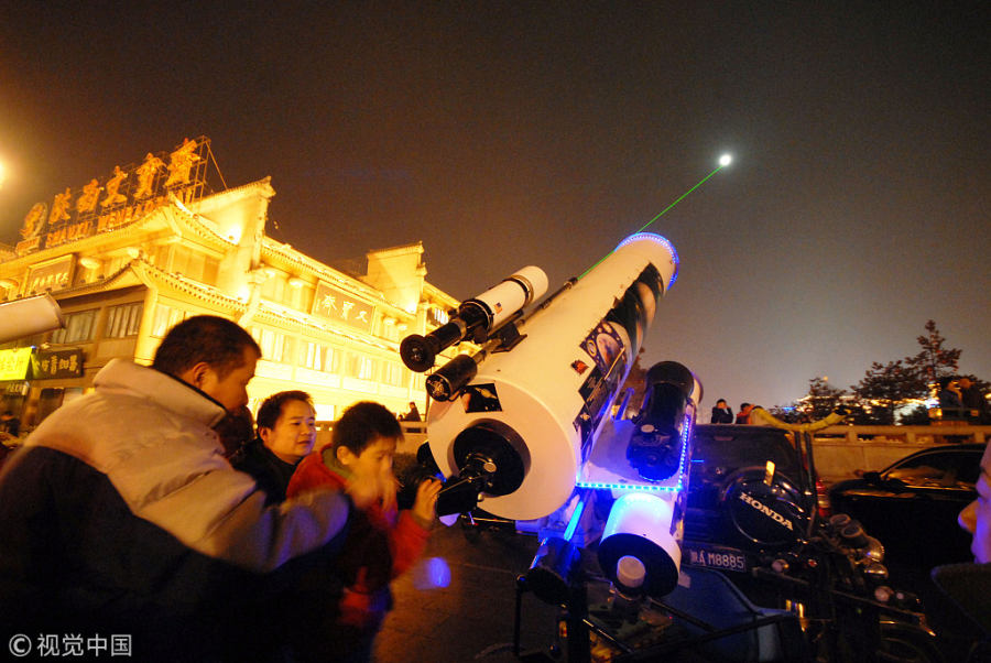 市民和游客晚上在路边利用望远镜看月亮.