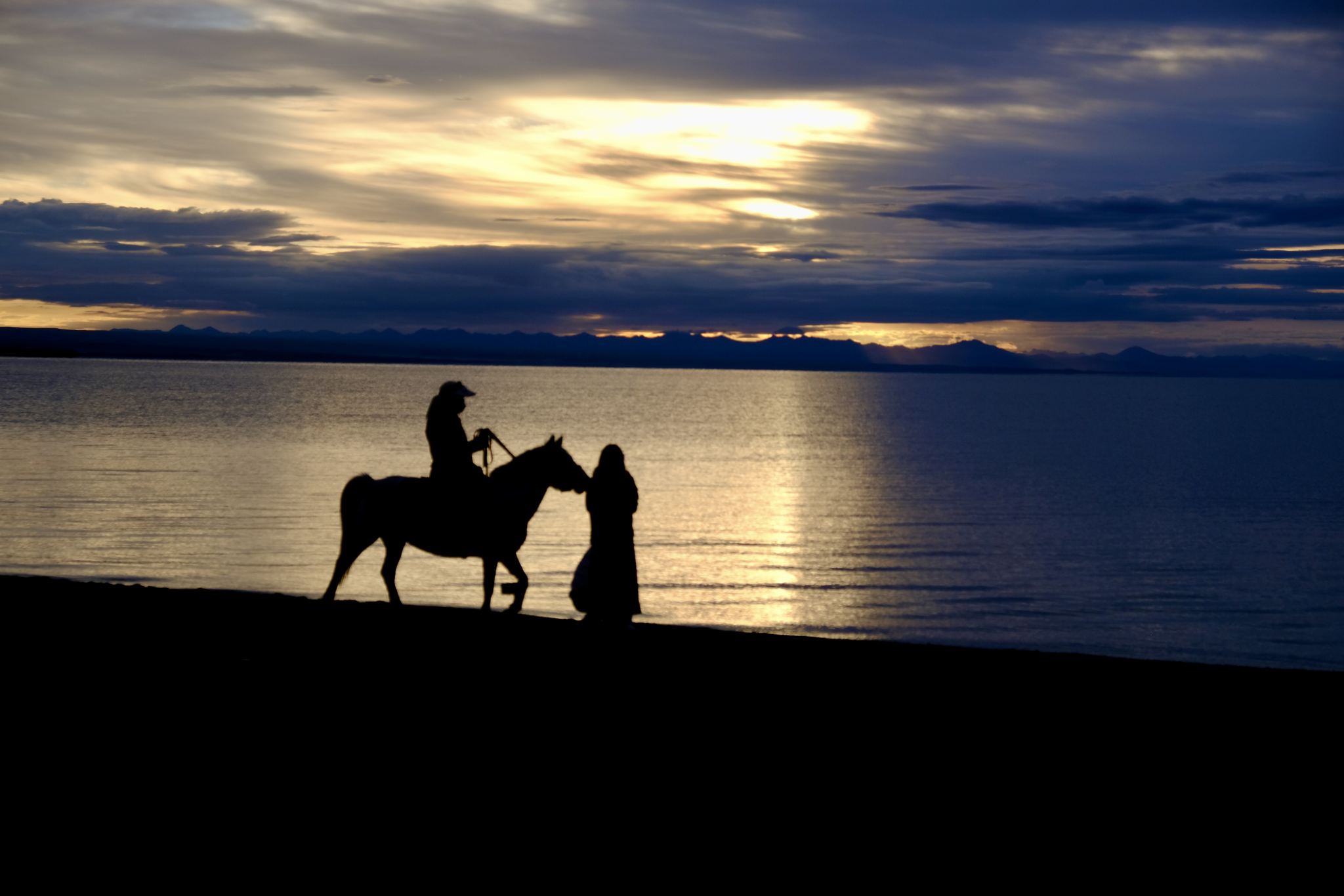 日出时青海湖边骑马的人们在天空的映衬下剪影